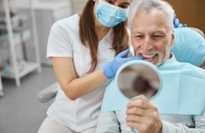 Dentist showing patient mirror — examining restored tooth with dental implant