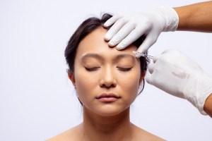 Woman receiving facial injection &mdash; gloved hands administering treatment to forehead